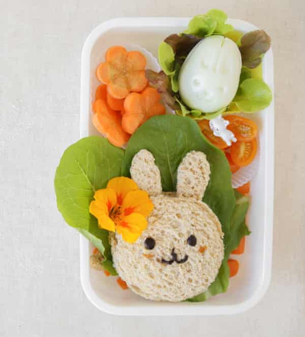 Una fiambrera con un bocadillo en forma de cabeza de conejo, zanahorias en flor y un huevo duro.