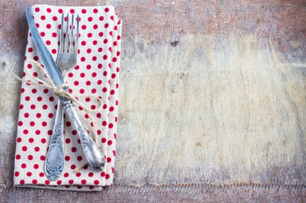 Un tenedor y un cuchillo atados con una cuerda en una servilleta de lunares rojos y blancos, sobre una mesa rústica.