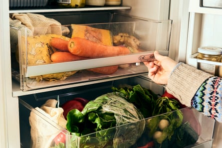 Una mano sacando un cajón para verduras del refrigerador lleno de zanahorias, calabaza y remolacha plateada.