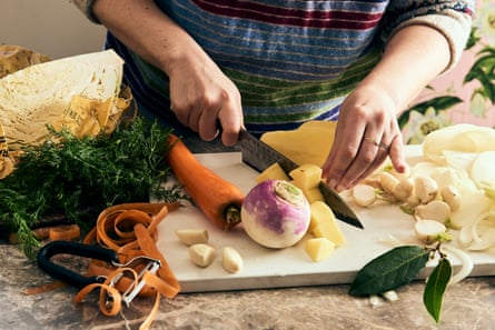 Las manos de una persona cortando una rutabaga en una tabla de cortar, que se espolvorea con zanahorias y eneldo.