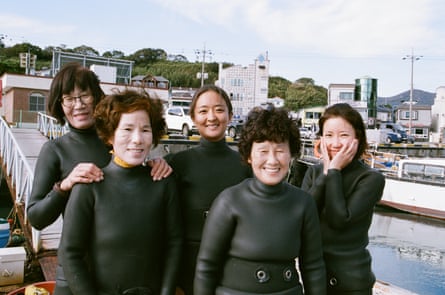 Cinco mujeres coreanas en monos se paran cerca del paseo marítimo y se ven felices juntas